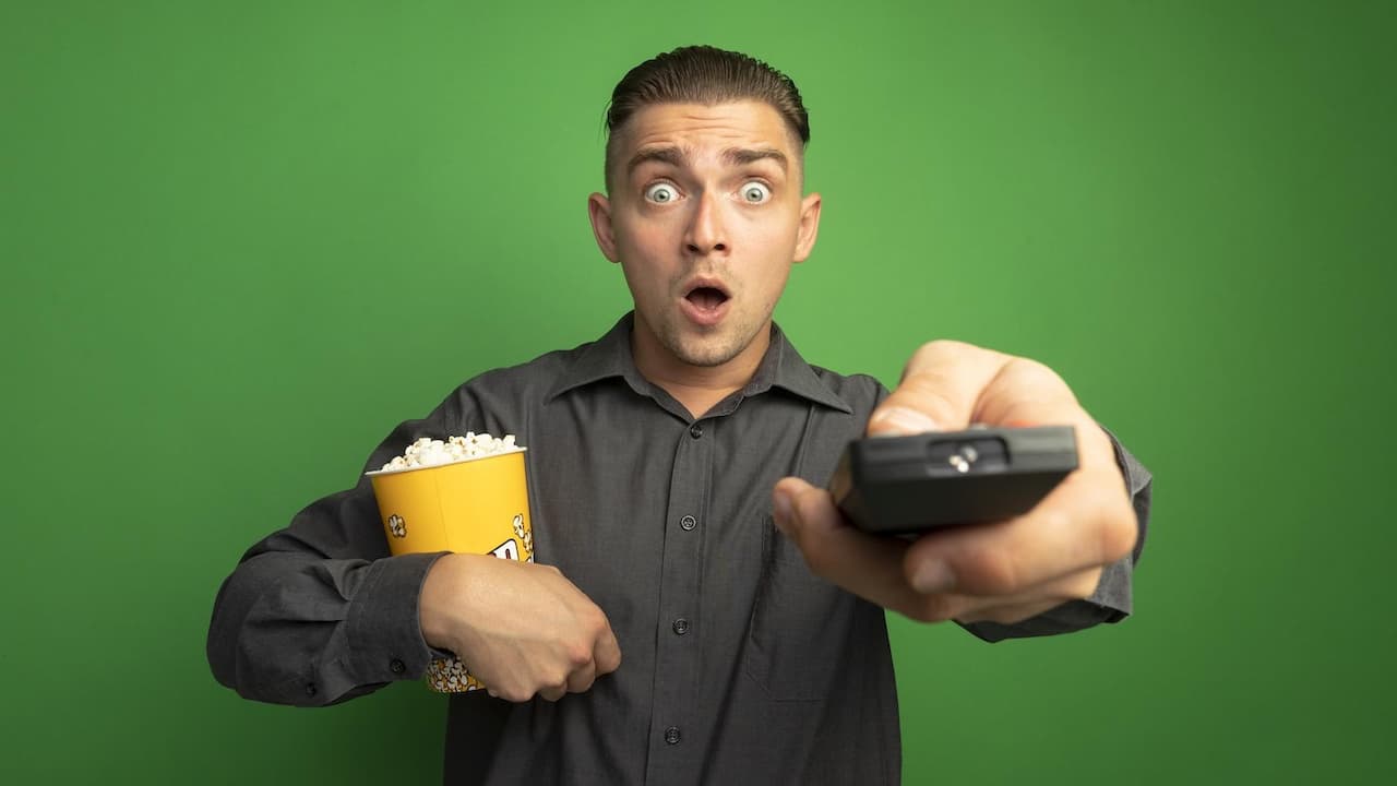 hombre-guapo-joven-en-camisa-gris-sosteniendo-un-cubo-con-palomitas-de-maiz-con-control-remoto-de-tv-mirando-al-frente-asombrado-parado-sobre-la-pared-verde hombre-guapo-joven-en-camisa-gris-sosteniendo-un-cubo-con-palomitas-de-maiz-con-control-remoto-de-tv-mirando-al-frente-asombrado-parado-sobre-la-pared-verde